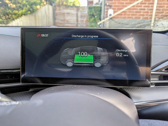 Photo of the driver's instrument display inside a BYD Seal electric car. It is showing the "Discharge in progress" screen, indicating that the car is being used to provide external mains power via the Vehicle to Load adapter. 0.2 kW of power is being used, and the battery is still at 100%.