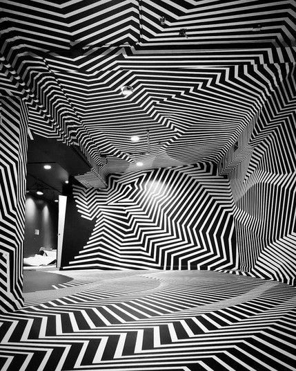 A black room covered in white tape lines creating jagged and curving indentations across the walls and floor.