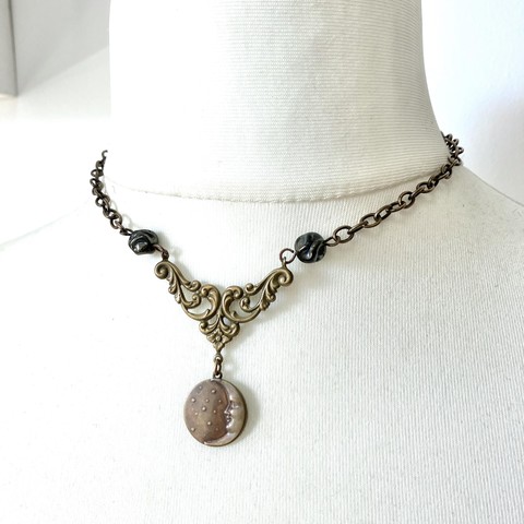 The rustic brass moon pendant necklace described in the previous photographs, this time photographed hanging on a white mannequin neck. Necklace is choker length, measuring 15.5 inches or 39 cm.