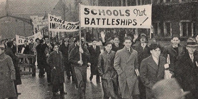 Grainy black and white photo of students marching for peace, 1935. Some of the signs read: "Schools, Not Battleships!" and "Strike Against Imperialism."