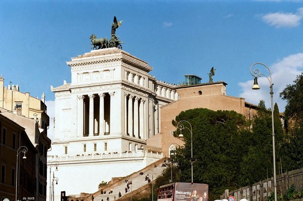 Farbfoto mit einem seitlichen Blick auf den Vittoriano, das Nationaldenmal für König Vittorio Emmanuele II in Rom, erbaut im neoklassizistischen Stil, mit der Quadriga der Einheit darauf. Rechts, größtenteils von Bäumen verdeckt, die Kirche Santa Maria in Aracoeli. Leica IIIc mit 90 mm Leitz Elmar auf Kodak Gold-Film.