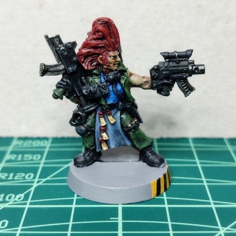 Miniatura de un cazarrecompensas de metal clásico de Necromunda. Es un tipo en pose de disparar una pistola bolter hacia su izquierda, mientras está cargando el peso sobre la pierna derecha, ligeramente flexionada y sostiene un rifle bolter hacia arriba con el brazo derecho apoyándolo en la cadera. Tiene un pelazo exagerado hacia arriba, en color rojo brillante. Viste un uniforme en verde militar con pantalones y chaqueta, que está entreabierta mostrando una camiseta en azul claro. Lleva múltiples bolsillos, cartucheras y grilletes colgando de varios sitios, incluyendo un respirador con tubo que se desplaza hacia atrás, todo en color negro. Lleva rodillera sólo en la derecha y botas militares negras.