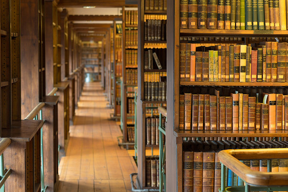 Blick in eine historische Bibliothek mit dunkel Holzregalen und ganz vielen alten „Schinken“.