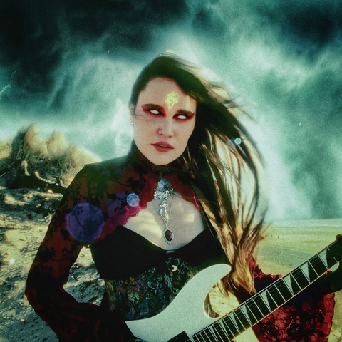 The image shows a person with long hair standing outdoors, holding a white electric guitar. The background features a dramatic, cloudy sky and a rugged landscape. The person is wearing a colorful, patterned outfit with a necklace that has a prominent pendant. The overall atmosphere of the image is artistic and dynamic, suggesting a music or rock-inspired theme.